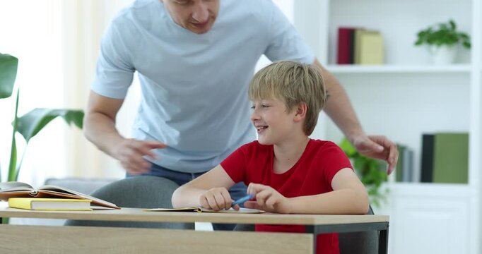 Father helping his son with homework at wooden table indoors, closeup