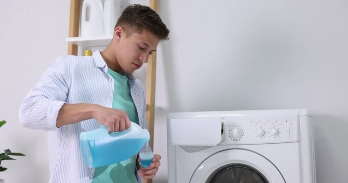 Man pouring liquid laundry detergent from bottle into cap near washing machine in room