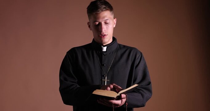 Priest in cassock reading Holy Bible on beige background