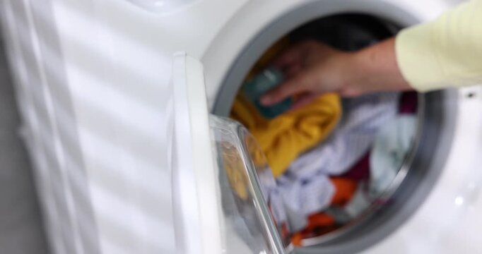 Woman loading washing machine and adding laundry detergent, closeup. Camera moving