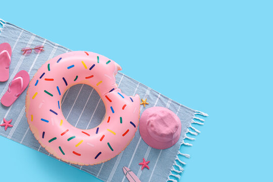 Pink donut inflatable ring with flip-flops, sunglasses, and bucket hat on a striped beach towel, summer vacation