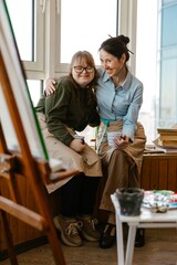 Two female artists smiling together in a colorful art studio © Drobot Dean