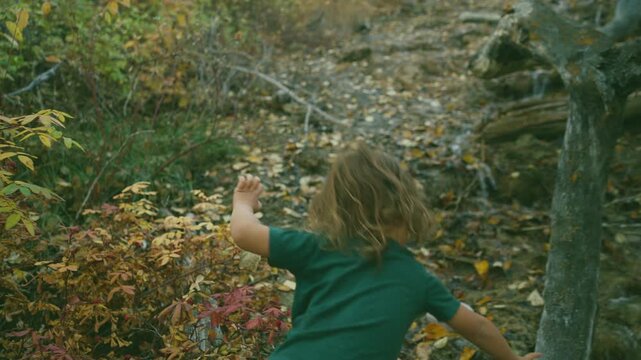 Young boy throwing a stone into a forest stream in autumn woods