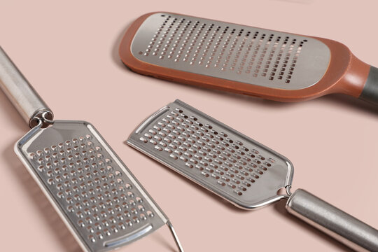 Stainless steel kitchen graters and zesters for food preparation on a light pink background