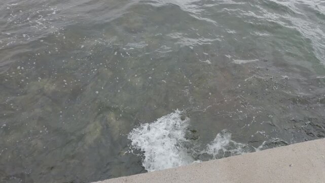 Close view of seawater waves lapping on shore tilting up to reveal fjord scenery