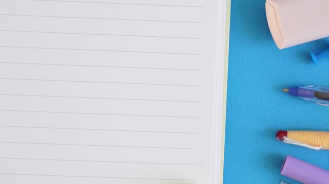Blue surface holds open notebook, pens, pencil, and paper clips. Items suggest creative work or study environment.