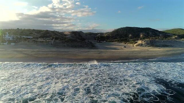 Drone pulls back over the ocean at Playa El Rinconcito on the East Cape of Baja California Sur, looking toward the arroyo before turning left to reveal more of the beach, a house, and the late afterno