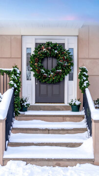 Front door wreath winter holiday Christmas decoration snowy steps festive porch evergreen garland snow covered suburban house seasonal decor evening light Christmas Concept