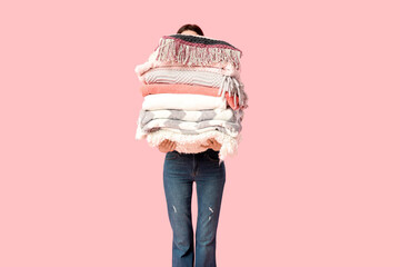 Naklejka premium Beautiful young woman with stack of different blankets and pillow on pink background