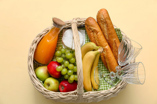 Wicker basket with tasty food and drink for picnic on beige background. Top view