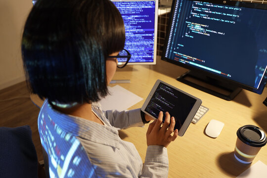 Young female programmer working with tablet computer in office at night, closeup