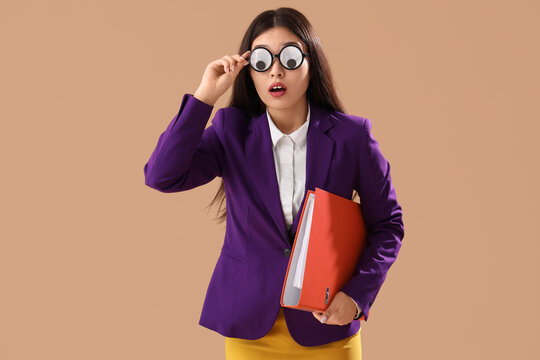 Young Asian businesswoman in funny disguise with folder on brown background