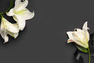 Fototapeta premium Frame made of beautiful lily flowers with black funeral ribbon on dark background