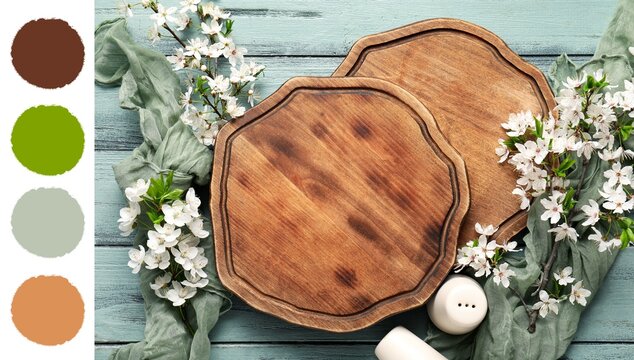 Two rustic wooden cutting boards with white cherry blossoms and a green cloth on a blue wooden table, the empty boards provide ample copy space for culinary designs or recipe layouts
