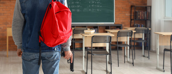 Student with red backpack holding a gun in a classroom, school violence and safety concern, Serious...