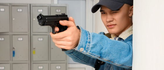 Fototapeta premium Young man in a baseball cap aiming a handgun in a school hallway with lockers, school violence and security
