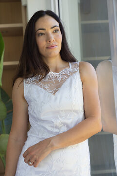 Female standing near glass door at home wearing embroidered dress with lace yoke showing ring