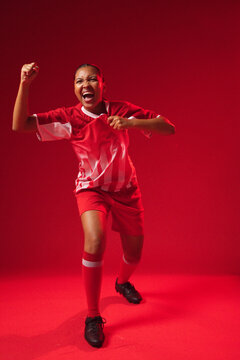 Female athlete shouting, raising fist, pulling jersey in studio with red jersey, black cleats