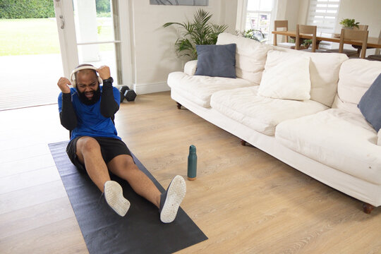 African American man exercising on yoga mat in living room wearing athletic clothes, copy space