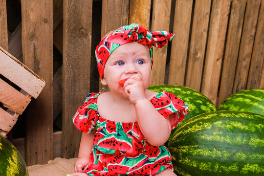 Little girl in watermelon print clothes sitting between watermelons