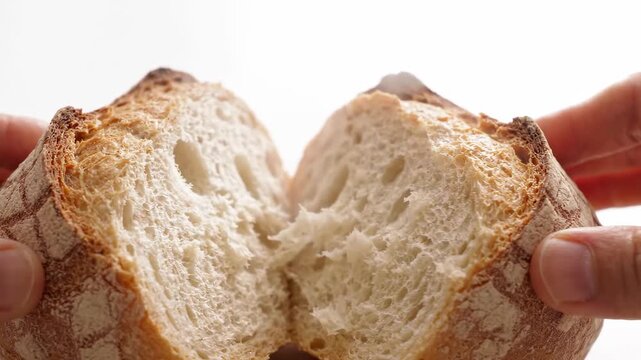 Hands breaking a crusty artisan loaf of bread showing the soft white crumb inside, perfect for food blogs or bakery promotions