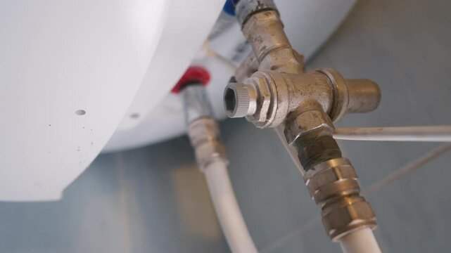 Water Heater Pipe Fitting Close Up: Brass Valve Connection with Flexible Hoses Under Boiler | Plumbing Installation and Repair Work | Slow Orbit Camera Movement Around Focused Valve