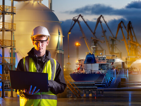 LNG terminal. Engineer uses a laptop to manage liquefied natural gas storage and maritime loading operations as an LNG carrier arrives at the port.