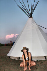 Woman sits beside white teepee at dusk © ExploringandLiving