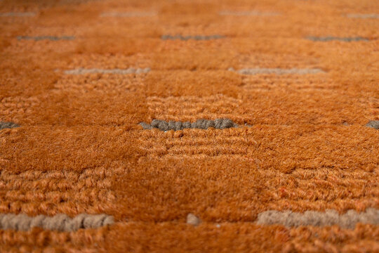 Close-up of an orange shag rug showing soft, plush texture and subtle tufted pattern. Warm ochre tones and tactile pile convey comfort, retro style,
