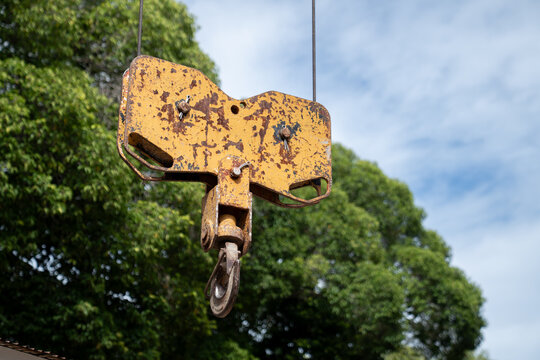 An old yellow crane sheave block with a steel hook hangs outdoors.