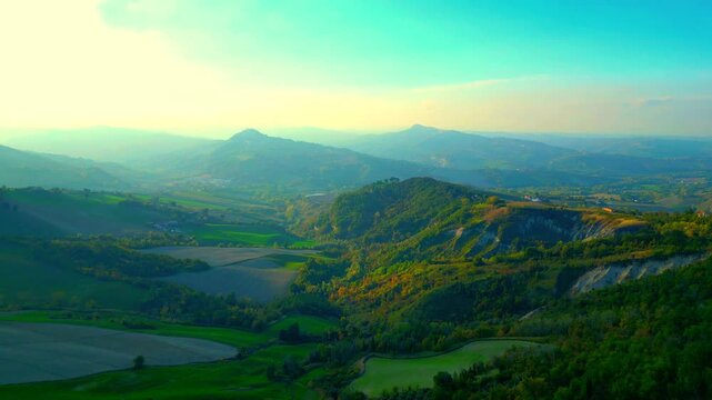Sumptuous aerial push-in pan right shot from near Santa Vittoria in Matenano, green peaks, ravines, atmosphere imbued with spiritual quality, while hazy mountains lie in the background, under the sky
