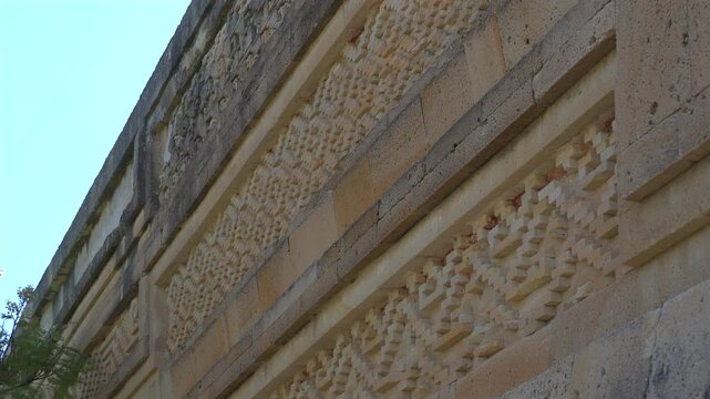 Static low angle shot of detailed ancient Zapotec geometric stone fretwork and carvings on a wall facade at Mitla archaeological site in Oaxaca, Mexico.