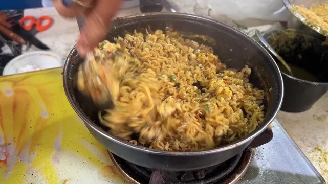 A dynamic close-up shot of egg-fried Maggi instant noodles being cooked over high heat at a roadside dhaba, packed with scrambled eggs, fresh vegetables, and Indian spices, India.