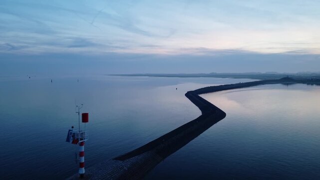 West-Terschelling, Terschelling, Friesland, Netherlands, revealing the harbor breakwater, navigation beacon, calm Wadden Sea waters and evening light, drone forward flyover.
