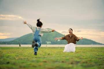 excited preschool child girl running into her mother's open arms on grass field near the river with mountain © geargodz