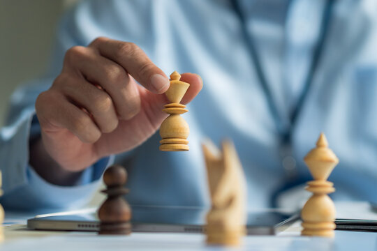 Close-up of office worker holding chess piece planning business strategy at desk with tablet and reports.