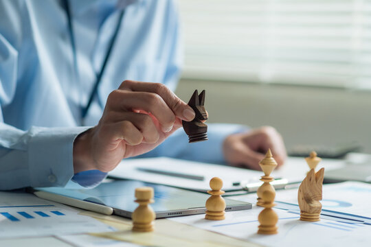 Close-up of office worker holding chess piece planning business strategy at desk with tablet and reports.