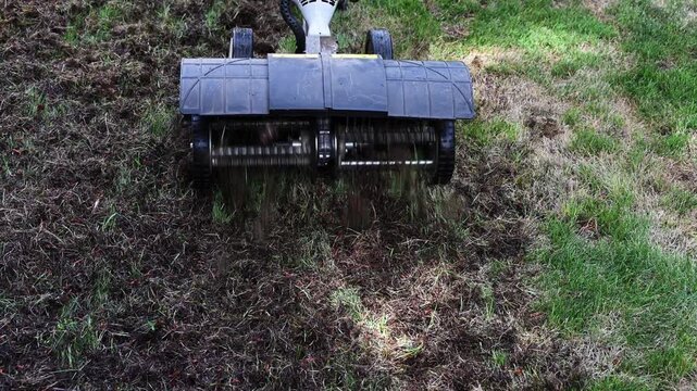Gas powered dethatcher machine being used to clean up dead grass, moss, and other organic material from grass lawn, landscaping maintenance
