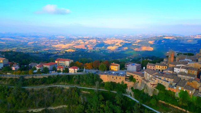 High-rise aerial push-in shot in Santa Vittoria in Matenano, stunning views of the landscapes surrounding the town centre with typical Marche hillscapes of thickets, fields and meadows, hazy horizon