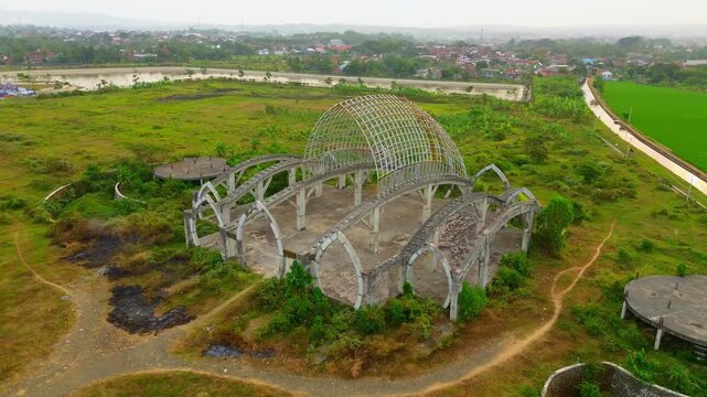 Aerial view of the Masjid Agung Purwokerto Seribu Bulan Sabit under construction with concrete arches and steel framework in Purwokerto, Central Java, Indonesia.