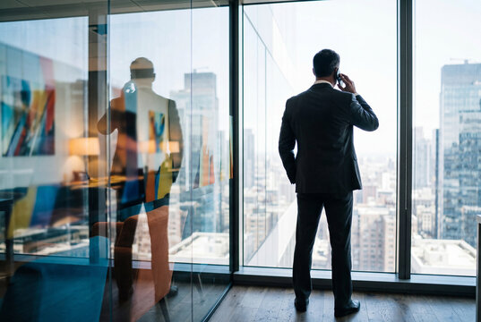 Corporate executive talking on mobile phone looking out city window