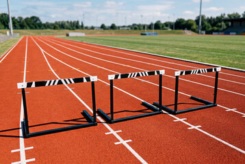 Naklejka premium Athletic hurdles lined up on red running track at empty stadium