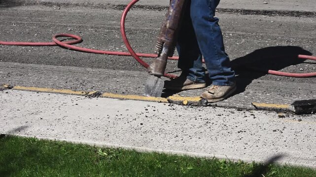 Construction worker using jack hammer to break up old asphalt as part of road repaving infrastructure project
