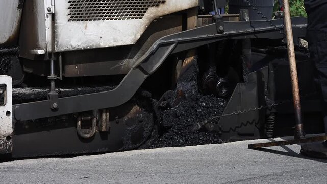 Closeup of auger assembly, auger drive box and helical auger, flights, screws, of an asphalt paver with hot fresh asphalt moving inside
