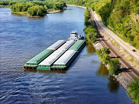 Aerial view of a tug boat with barges waiting outside the main channel next to the Mississippi shoreline.
