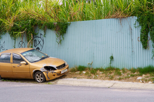 Damaged car parked beside corrugated metal fence