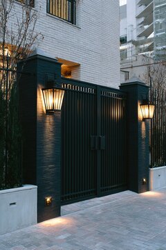 Elegant black metal entrance gate of a luxury house with lit lamps