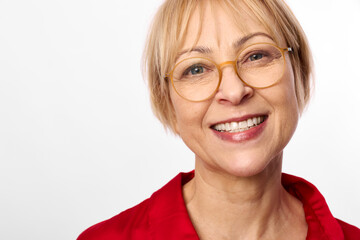 Obraz premium Woman smiling with glasses in a closeup portrait, blond hair, red shirt, bright studio light, friendly expression, calm confident mood, plain white background, clean minimal