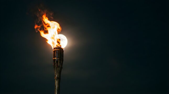 Burning tiki torch lit against a bright full moon at night