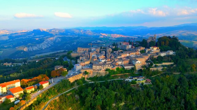 Stunning aerial pullback truck right pan left pedestal up shot from Santa Vittoria in Matenano, the high promontory full of thickets and trees where the town centre lies with its historic buildings